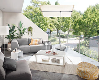 Moderne Außenterrasse mit grauen Sofas, weißem Couchtisch, gelbem Ottomanen, Pflanzen und Blick auf Bäume und Straße.