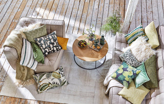 Gemütliches Wohnzimmer mit gemusterten Kissen, einem Couchtisch aus Holz und Getränken auf einem hellen Teppich über einem Holzboden.
