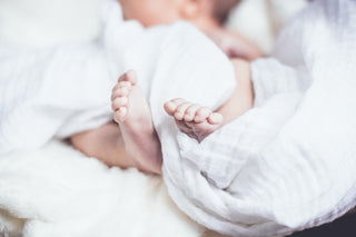Nahaufnahme der Füße eines Babys, das in eine weiche, weiße Decke eingekuschelt ist.