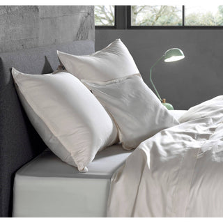 Modernes Schlafzimmer mit weißer Bettwäsche, drei Kissen, einer grünen Lampe und einem großen Fenster mit Blick auf Bäume.