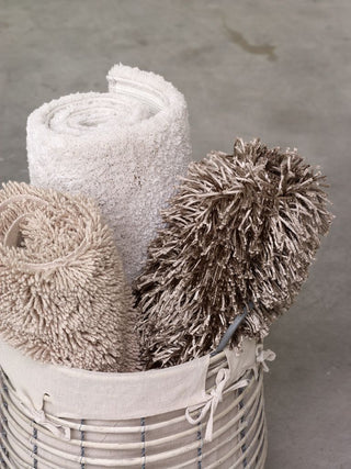 Gerollte beige und braune Teppiche in einem Weidenkorb mit Stoffbezug auf einem Betonboden.