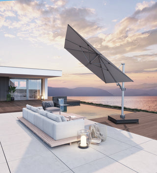 Moderne Terrasse mit großem Sonnenschirm, weißem Sofa und Laterne und herrlichem Meerblick bei Sonnenuntergang.