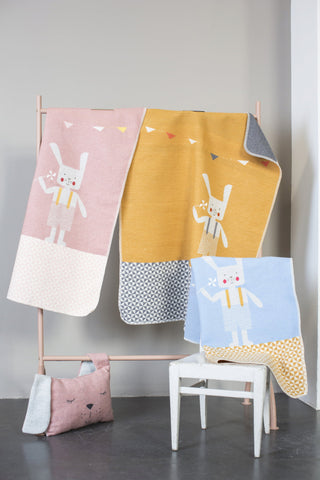 Kinderdecken mit Hasenmotiven hängen an einem Ständer, daneben liegt ein rosa Kissen auf einem Stuhl.