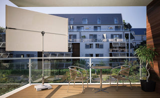 Moderner Balkon mit einem kleinen Tisch, zwei Stühlen und einem großen Sonnenschirm mit Blick auf ein Wohnhaus und ins Grüne.