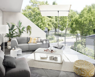 Moderne Terrasse mit grauen Sofas, weißem Tisch, gelbem Kissen und Pouf sowie Sonnenschirm mit Blick ins Grüne.