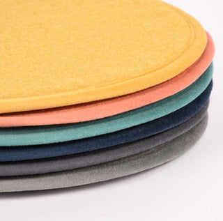 Stapel runder Tischsets aus Filz in verschiedenen Farben: Gelb, Koralle, Blaugrün, Marineblau und Grau auf einer weißen Oberfläche.