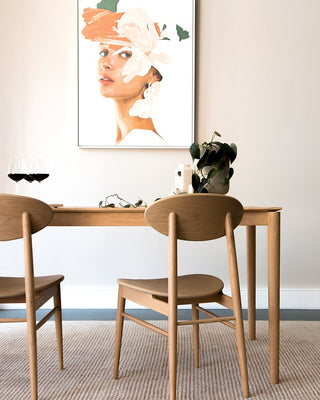 Minimalistisches Esszimmer-Setup mit Holztisch und -stühlen, Weingläsern, Pflanze und Kunstwerk an einer beigen Wand.