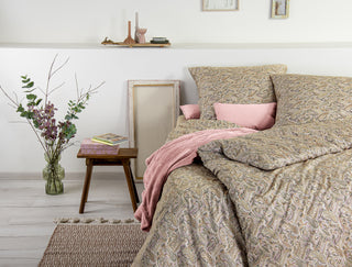Gemütliches Schlafzimmer mit Bettwäsche im Paisleymuster, rosa Akzenten und einem Nachttisch mit Büchern und einer Vase mit Zweigen.