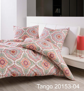 Die Janine Bettwäsche Seersucker Tango 20153 rot zeigt ein farbenfrohes, kompliziertes Muster auf der Bettwäsche neben einer roten Lampe und Kissen und kombiniert modernes Design mit pflegeleichten Eigenschaften.