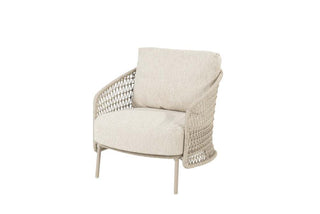 Der 4Seasons Living Sessel Puccini Latte, ein beige gepolsterter Sessel mit geflochtenen Seitenteilen und dünnen, leicht nach rechts geneigten Beinen, verkörpert modernes Design.