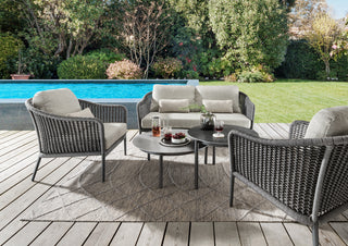Das DeVries Lounge-Set Lanzarote Rope grau umfasst vier Korbstühle, ein Sofa und zwei Tische, die an einem Pool inmitten üppiger Vegetation aufgestellt sind. Mit einem eleganten Seilgeflecht-Design mit langlebigen Aluminiumgestell-Rahmen kombiniert dieses Terrassenset Stil und Robustheit.