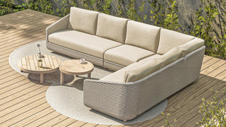 Das 4Seasons Lounge-Set Casanova Rope Latte von Zeo Living, ein L-förmiges beiges Outdoor-Lounge-Set mit wetterfesten Kissen und einem Seil-Muster-Design, steht auf einer Terrasse mit zwei runden Holztischen und üppigem Grün im Hintergrund.