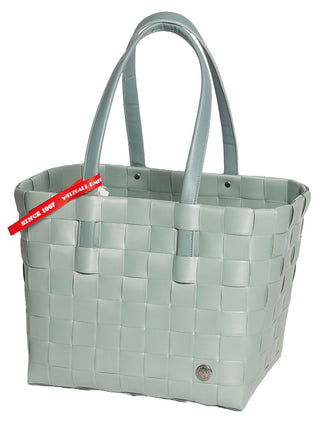 Der Witzgall Shopper 5050-57/0U Grün mit Lederhenkel ist eine gewebte hellgrüne Einkaufstasche mit zwei Griffen und einem kleinen runden Metallemblem. Ein rotes Etikett an einem Griff hebt das robuste, pflegeleichte Material hervor, das sowohl Haltbarkeit als auch Komfort gewährleistet.