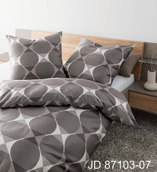 Luxuriöse Janine Bettwäsche Mako-Satin J.D. 87103 in grauen geometrischen Mustern ziert ein Bett mit einem hölzernen Kopfteil und einem kleinen Beistelltisch und schafft so ein zeitloses Design. Code: JD 87103-07.