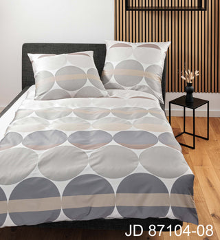 Minimalistisches Schlafzimmer mit Janines Mako-Satin-Bettbezug J.D. 87104-08 mit geometrischem Kreismuster, kombiniert mit luxuriösen Baumwollkissen und einem kleinen Beistelltisch mit Dekor.
