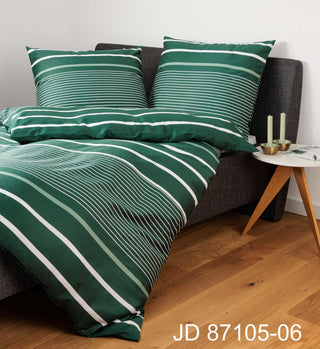 Janines J.D. Bettwäsche Mako-Satin 87105-06 Grün ziert ein dunkles Bett, gepaart mit einem kleinen hölzernen Beistelltisch mit Kerzen.