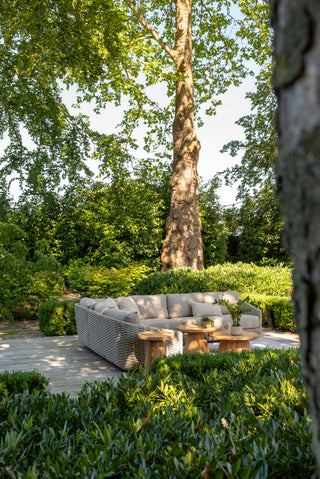 Sitzbereich im Freien mit dem Zeo Living 4Seasons Lounge-Set Casanova Rope Latte im Seilmuster-Design, begleitet von runden Holztischen. Üppige grüne Bäume und Büsche umgeben den Raum, während wetterfeste Kissen für Komfort bei jedem Wetter sorgen.