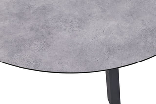 Nahaufnahme eines Kettler Ausziehtischs 120/170x120cm mit einer runden HPL-Tischplatte mit grauer Betonstruktur und einem pulverbeschichteten Aluminiumrahmen im Hintergrund.