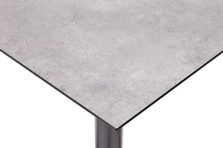 Nahaufnahme des KETTLER Gartentischs Tube, einem grauen, minimalistischen Tisch mit einer HPL-Betonoberfläche und einem einzelnen anthrazitfarbenen Aluminiumbein.