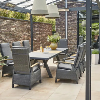 Auf einer Außenterrasse steht der Siena Garden Ausziehtisch Lindos, ein wetterbeständiger, FSC-zertifizierter Esstisch aus Teakholz von Siena Garden, begleitet von acht Korbstühlen, Hängelampen und Topfpflanzen unter einer Glaspergola.
