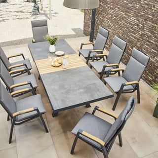 Das Siena Garden Lindos Esstisch-Set besteht aus einem grauen Ausziehtisch (205/265x100cm) und acht gepolsterten Stühlen auf einer Terrasse, geschmückt mit Blumen und Geschirr. Hergestellt aus FSC-zertifiziertem Teakholz bietet es eine elegante und wetterbeständige Note für dauerhaften Stil.