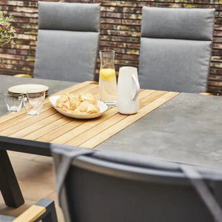 Der Ausziehtisch Lindos von Siena Garden aus FSC-zertifiziertem Teakholz von Siena Garden präsentiert eine wetterbeständige Oberfläche aus Holz und Schiefer mit Gebäck, einem Krug, Gläsern und einer Vase. Drei gepolsterte Stühle vervollständigen diese einladende Essecke im Freien.