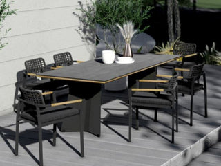 Auf einer einladenden Terrasse thront ein rechteckiger Tisch mit sechs Zebra Gartenstühlen Yobex Rope anthrazit, die ergonomischen Sitzkomfort bieten. Eine Vase mit Pampasgras und zwei Tassen, gefertigt aus wetterfestes Rope-Material, runden die Szene ab, perfekt geeignet für Outdoor-Bedingungen.
