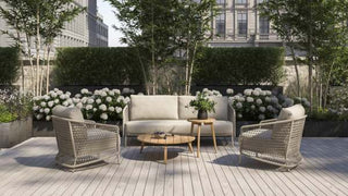 Ein Außensitzbereich mit einem 4Seasons 3-Sitzer-Sofa Puccini Latte, zwei Korbstühlen mit einzigartigem Rope-Geflecht, einem runden Tisch und üppigem Grün im Hintergrund schafft eine moderne Design-Oase.